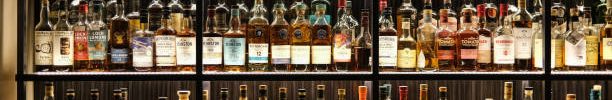 Various whiskey bottles on shelves in a bar. Premium Whisky Shipping Policy